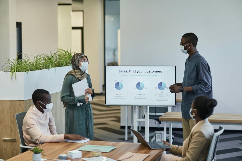Business professionals in masks discuss customer profiles in a modern office setting.